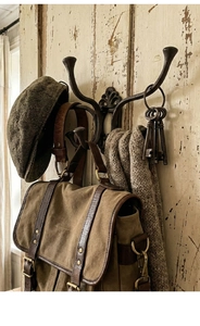 Vintage cast iron hook with grey wool hat and leather canvas bag on rustic wooden door