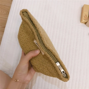 Close-up of khaki woven makeup pouch with silver zipper and simple logo detail