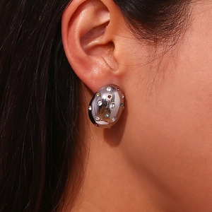 Macro detail of oval silver earrings with colorful zircons worn on model ear