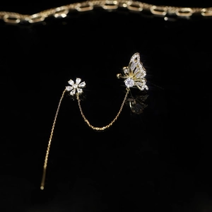 Detail of gold butterfly and flower zircon ear cuff with tassel chain on black background
