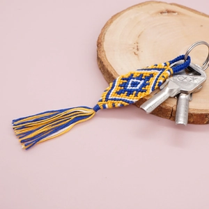 Ethnic bohemian woven key ring with diamond patterns, blue yellow tassels on wood base