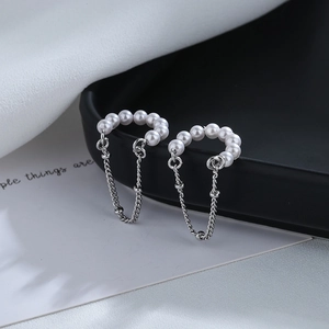 Detail of gold-plated pearl chain tassel ear cuffs hanging on a black ceramic tray