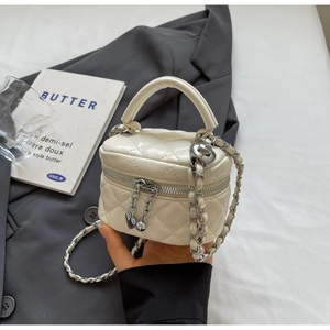 Detail of quilted cream mini vanity bag featuring a chain strap and metal ball adjuster