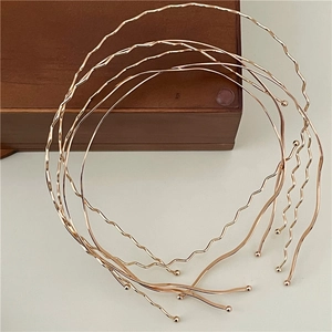 Close-up of golden wavy metal headbands stacked on a white minimalist background