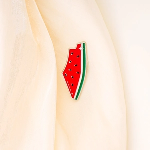 Close-up of a small watermelon enamel pin with gold trim pinned to silk fabric