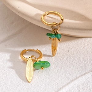 Elegant gold leaf earrings with green stone charms in a luxurious lifestyle setting
