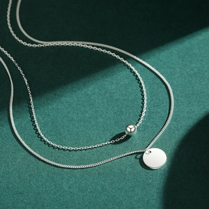 Double-layered 925 sterling silver necklace with beads and a round pendant on green texture
