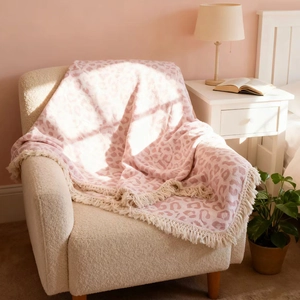 Detailaufnahme der rosa Babydecke mit Leopardenmuster und Fransen auf dem Sofa