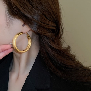 Close-up of gold-plated brushed metal hoop earrings worn by a model in a minimal style