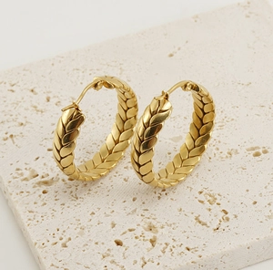 Détail de boucles d'oreilles créoles tressées en or 18K sur une pierre de travertin naturelle