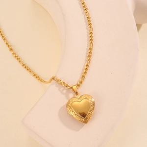 Detail of 18k gold plated heart locket pendant on Figaro chain over stone background