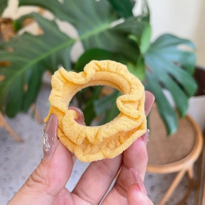 Elegant yellow fabric scrunchie with ruffle edge texture held in hand for hair styling
