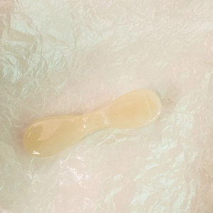 Détail d'une spatule cosmétique en résine jaune crème sur fond de papier texturé blanc