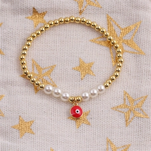 Détail du bracelet avec perles dorées, perles blanches et charme œil maléfique rouge
