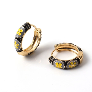 Close-up of golden hoop earrings with black enamel and yellow flower pattern