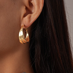 Close-up of a model wearing minimalist golden hollow crisscross earrings with metallic finish