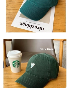 Close-up of a blackish green cotton baseball cap with white heart embroidery on a table