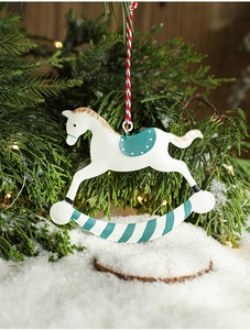 Detail of hand-painted metal rocking horse ornament hanging on a snowy Christmas tree branch