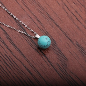 Close-up of a natural turquoise sphere pendant with silver chain on wood background