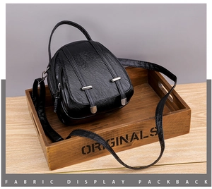Close-up of black retro leather crossbody bag with silver hardware in a wooden tray
