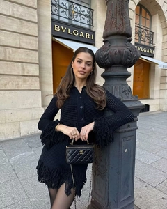 Close-up of black knit dress featuring fringe trim on cuffs and hem with gold buttons