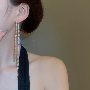Close-up of long silver tassel earrings with zircons on model against a warm background