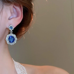 Detail view of oval blue gemstone earrings with white diamond halo on a model