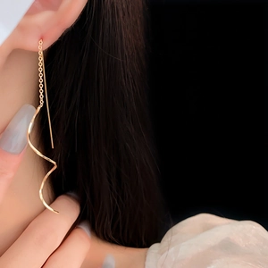 Vue détaillée de longues boucles d'oreilles spirales dorées portées sur un fond noir