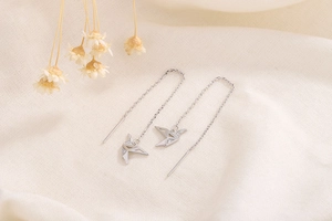 Detailed view of silver origami crane earrings with micro-inlaid zircons on linen fabric