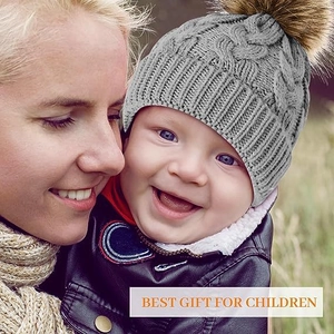 Close-up of light gray knit baby beanie with cable texture and brown faux fur pom-pom