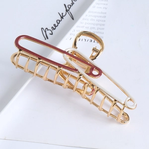 Detail of gold metal claw clip with red and white enamel finish on minimalist background