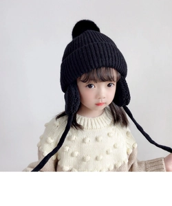 Detail of children's black winter knit hat featuring warm earflaps and fuzzy pom-poms