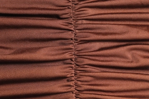 Detailed close-up of brown knitted fabric texture featuring ruching craftsmanship on the dress