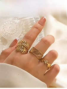 Detailed view of three gold-plated leaf rings worn on hand over elegant white silk