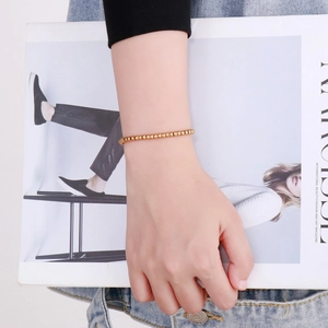Golden 4mm bead bracelet with lobster clasp worn by a model holding a fashion magazine