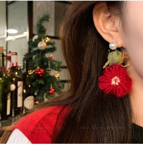 Detail of crochet Christmas flower earrings with red petals and green yarn ball on model