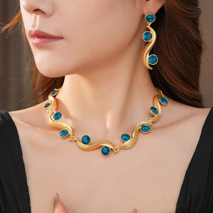 Close-up of gold wavy necklace and earrings set with blue gemstones worn by a model