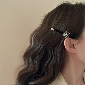 French vintage black camellia hair clip with pearl detail on elegant wavy brown hair