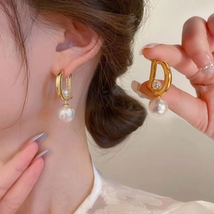 Modern gold D-shape metal earrings with large white pearl drop pendants on a model