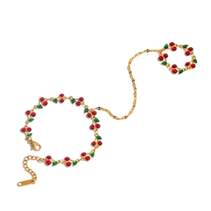 Detail of gold finger bracelet with red cherry charms and green leaves on white background
