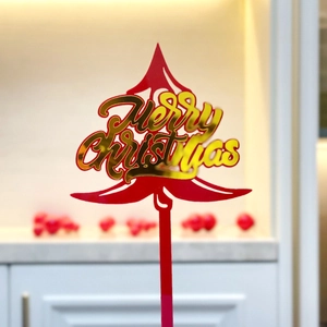 Close-up of red acrylic Christmas tree cake topper with shiny gold Merry Christmas text