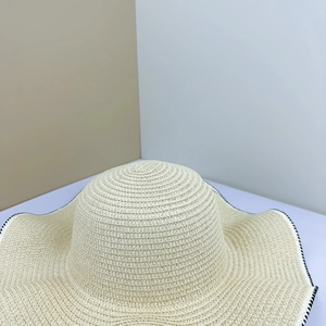 Detail of beige wide-brim straw hat featuring spiral weave and black-and-white stitched edge