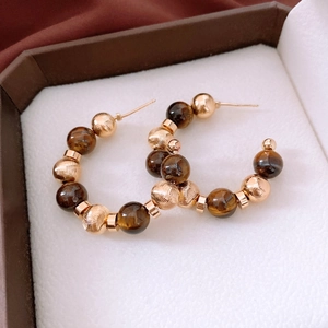 Macro shot of 16K gold-plated C-shape earrings with tiger eye beads in a jewelry box