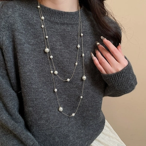 Detail of elegant double-layer pearl necklace with golden chain on grey sweater