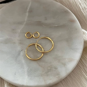 Minimalist gold round hoop earrings in two sizes displayed on white marble stone