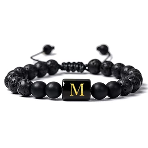 Détail du bracelet en pierre de lave avec initiale M dorée sur breloque polie