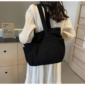Détail de la texture en velours côtelé noir du grand sac cabas en toile avec bandoulières
