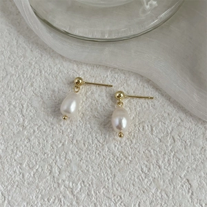Detail of freshwater pearl drop earrings with golden studs on textured white background