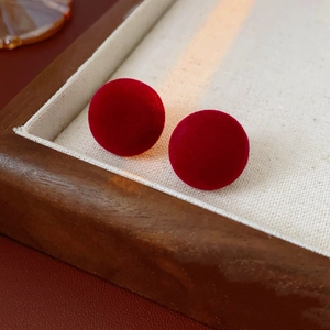 Close-up of red velvet spherical stud earrings with silver needle on wooden display tray