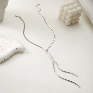 Macro detail of silver layered snake chain necklace with Y-shaped tassel on white tray
